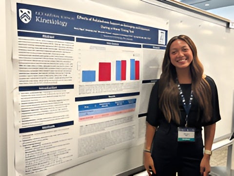 Student researcher smiling next to a research poster presentation during an academic showcase