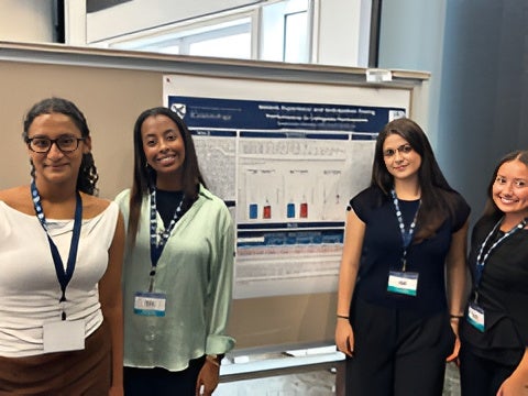 Group of student researchers posing together in front of their department research poster
