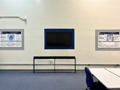 Wall-mounted television display flanked by research posters inside the Movement Behavior Lab